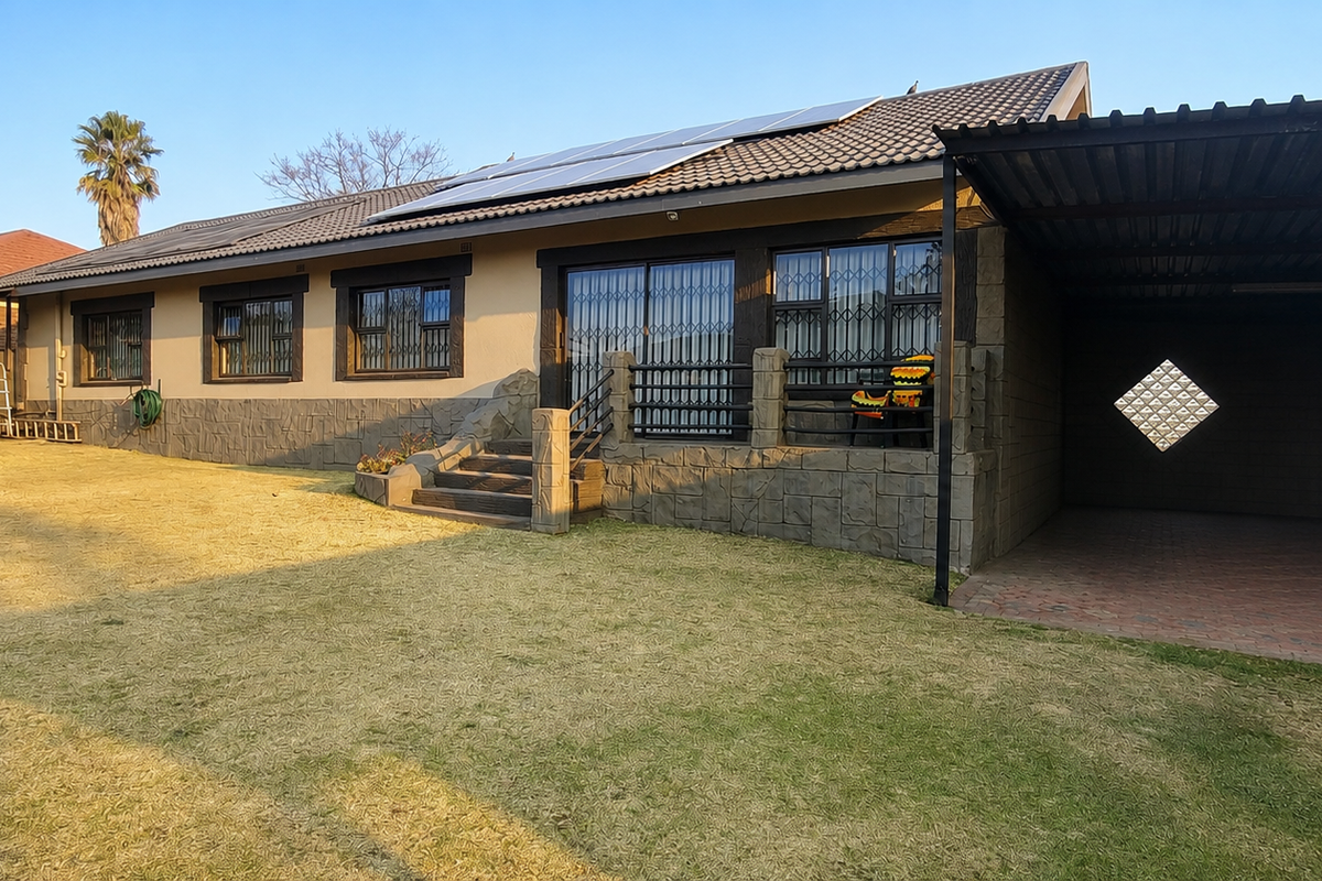 Rear view of the property featuring a spacious lawn, stone-clad facade, solar panels on the roof, and an attached carport with paved flooring.