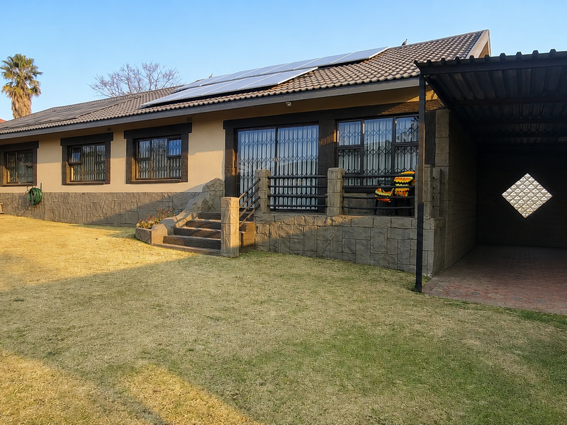 Rear view of the property featuring a spacious lawn, stone-clad facade, solar panels on the roof, and an attached carport with paved flooring.