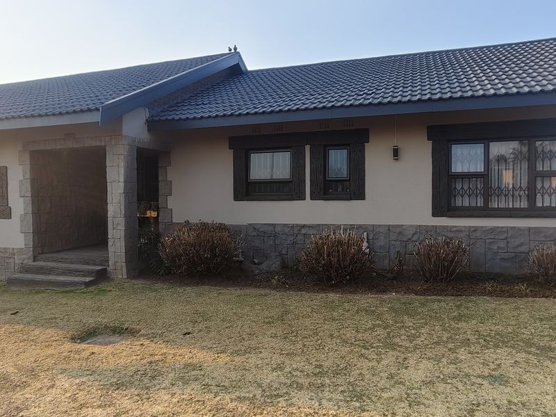 Front elevation of a single-story house featuring a tiled roof, stone cladding accents, and secure window bars.