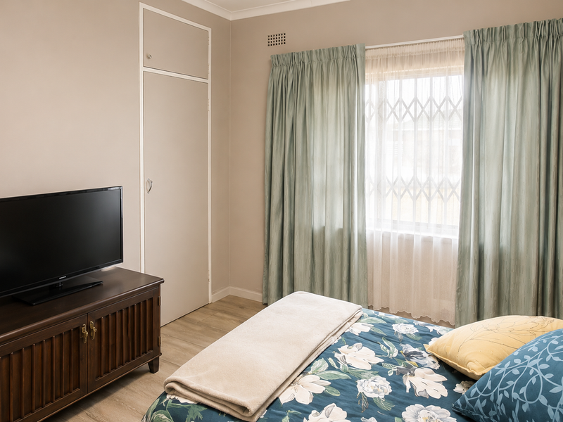 A well-maintained bedroom featuring laminate flooring, a built-in cupboard, and a window fitted with a security gate.