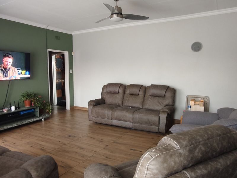 Spacious living room featuring wood-look tile flooring, a ceiling fan, and a prominent green accent wall.