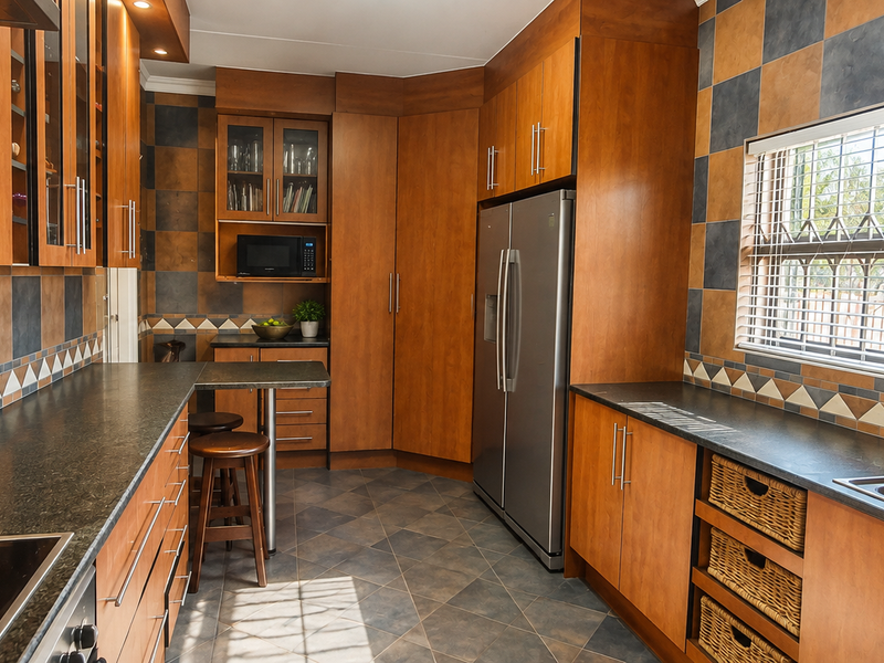 A functional kitchen featuring wood-tone cabinetry, dark laminate countertops, a built-in cooktop, and a double sink with a tiled backsplash.