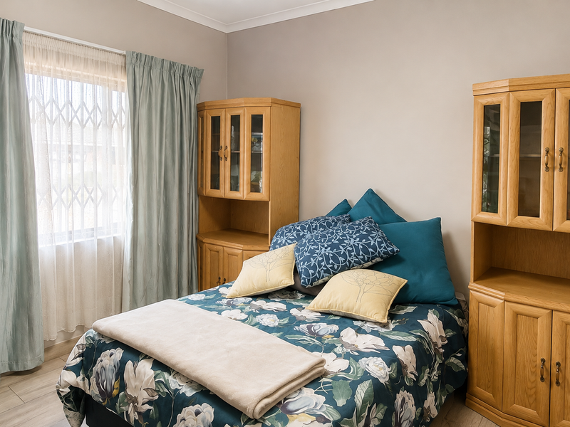 A well-maintained bedroom featuring laminate flooring, neutral wall tones, and a window fitted with a security gate.