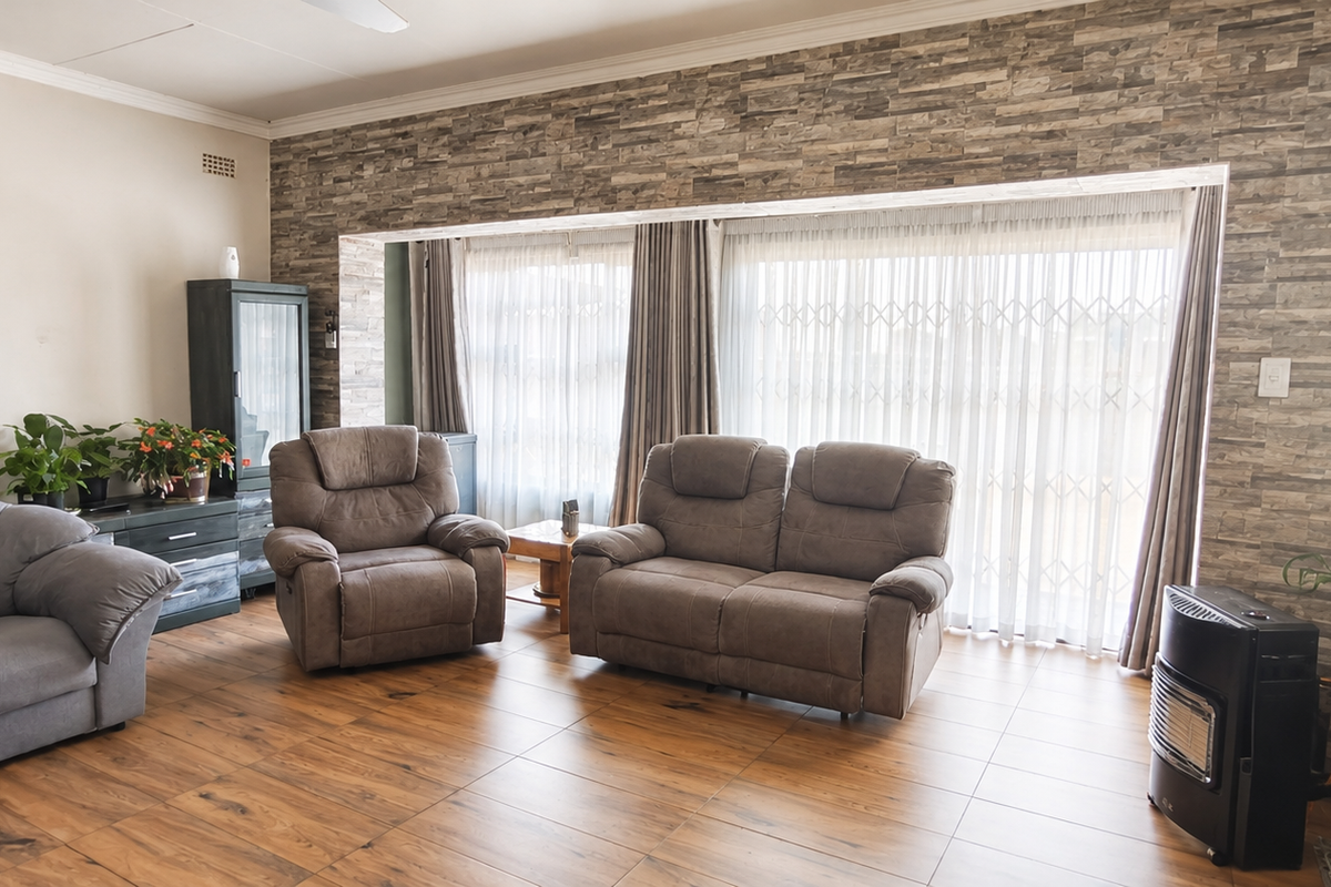 Spacious living room featuring a stone-cladding accent wall, tiled flooring, and large sliding glass doors with security gates for natural light.