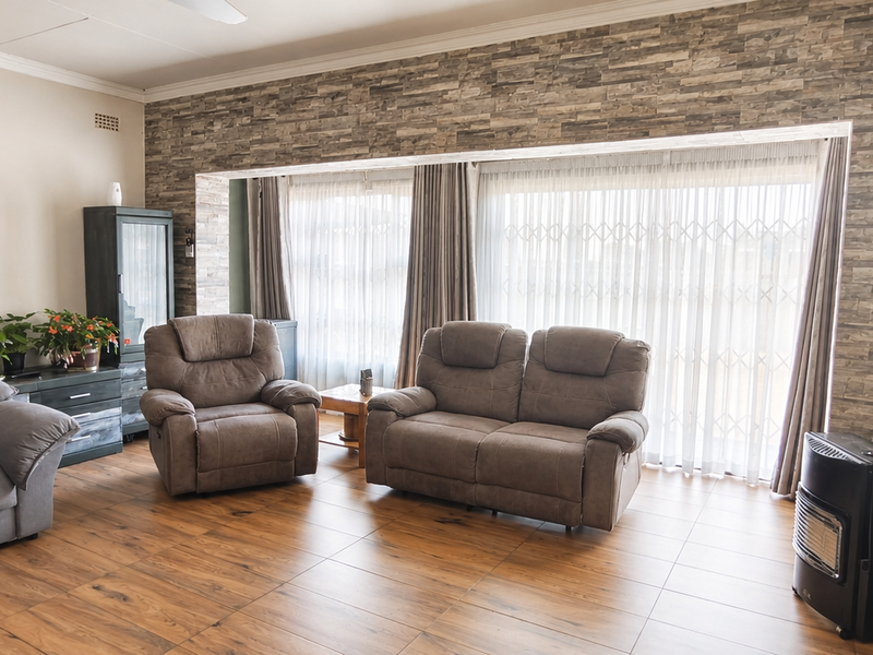 Spacious living room featuring a stone-cladding accent wall, tiled flooring, and large sliding glass doors with security gates for natural light.