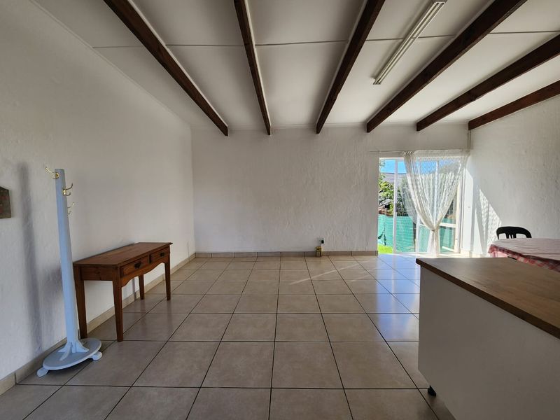 Spacious open-plan living area featuring exposed timber ceiling beams, neutral ceramic floor tiles, and direct access to the garden through a sliding glass door.