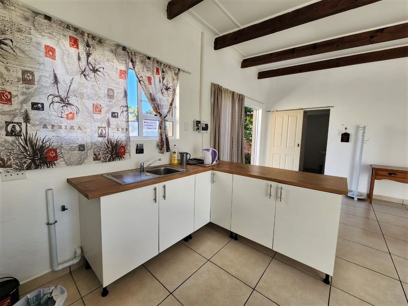 A functional kitchen area featuring white cabinetry, wooden countertops, exposed timber ceiling beams, and tiled flooring with direct access to an outdoor space.