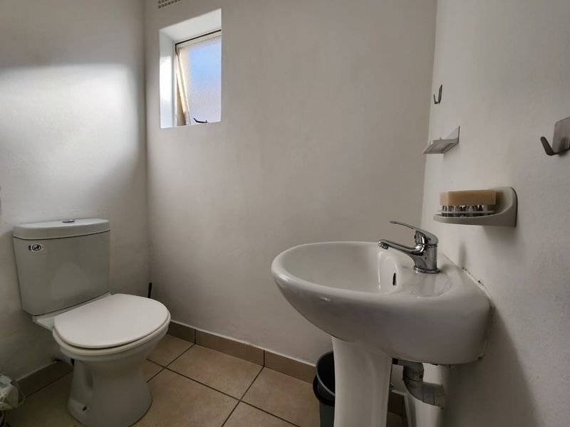 A functional guest bathroom featuring a pedestal basin, standard toilet, tiled flooring, and a small top-hung window.