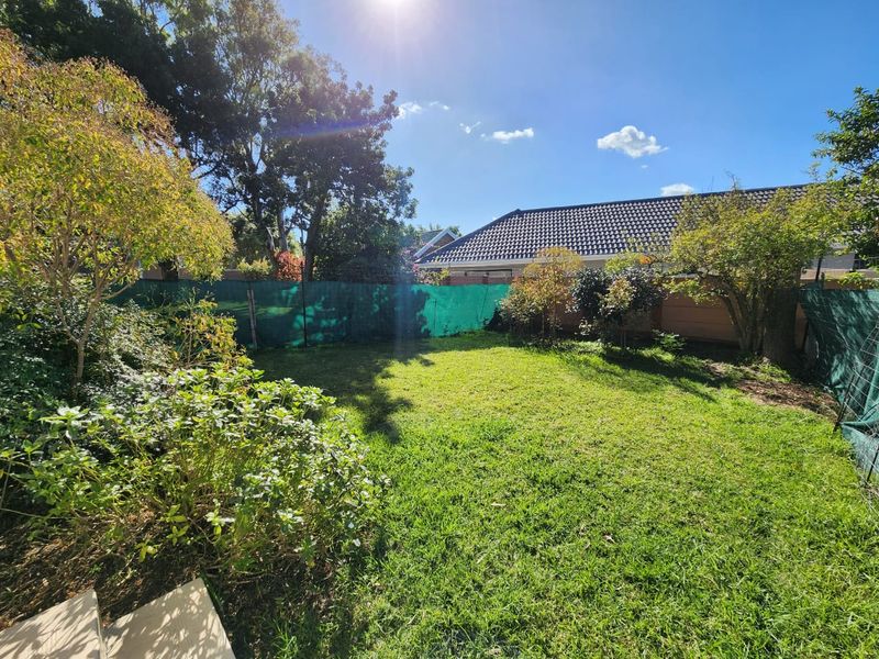 A private rear garden featuring a grass lawn, mature trees, and perimeter boundary fencing.