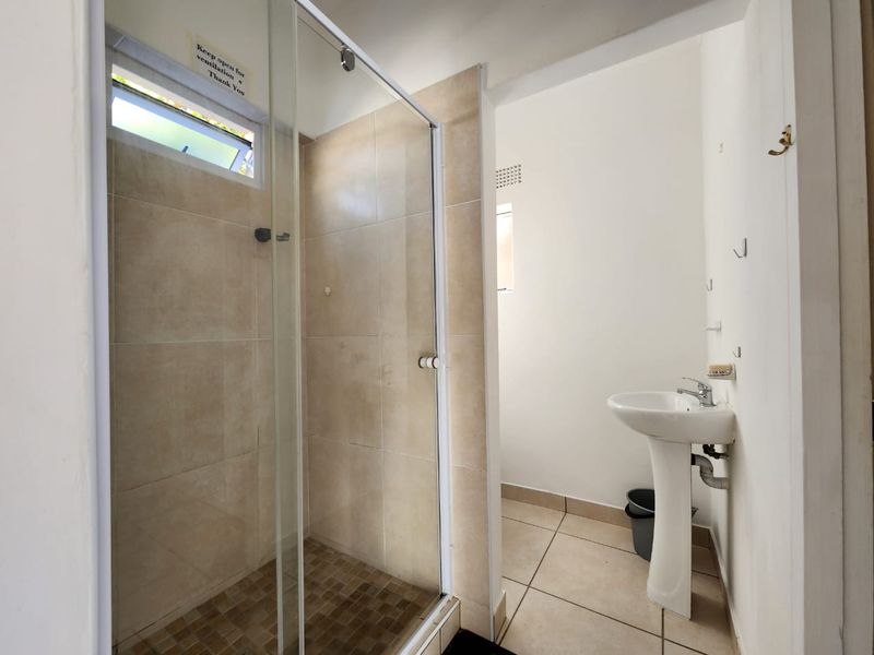 A functional bathroom featuring a glass-enclosed shower, pedestal washbasin, and neutral ceramic tiling throughout.
