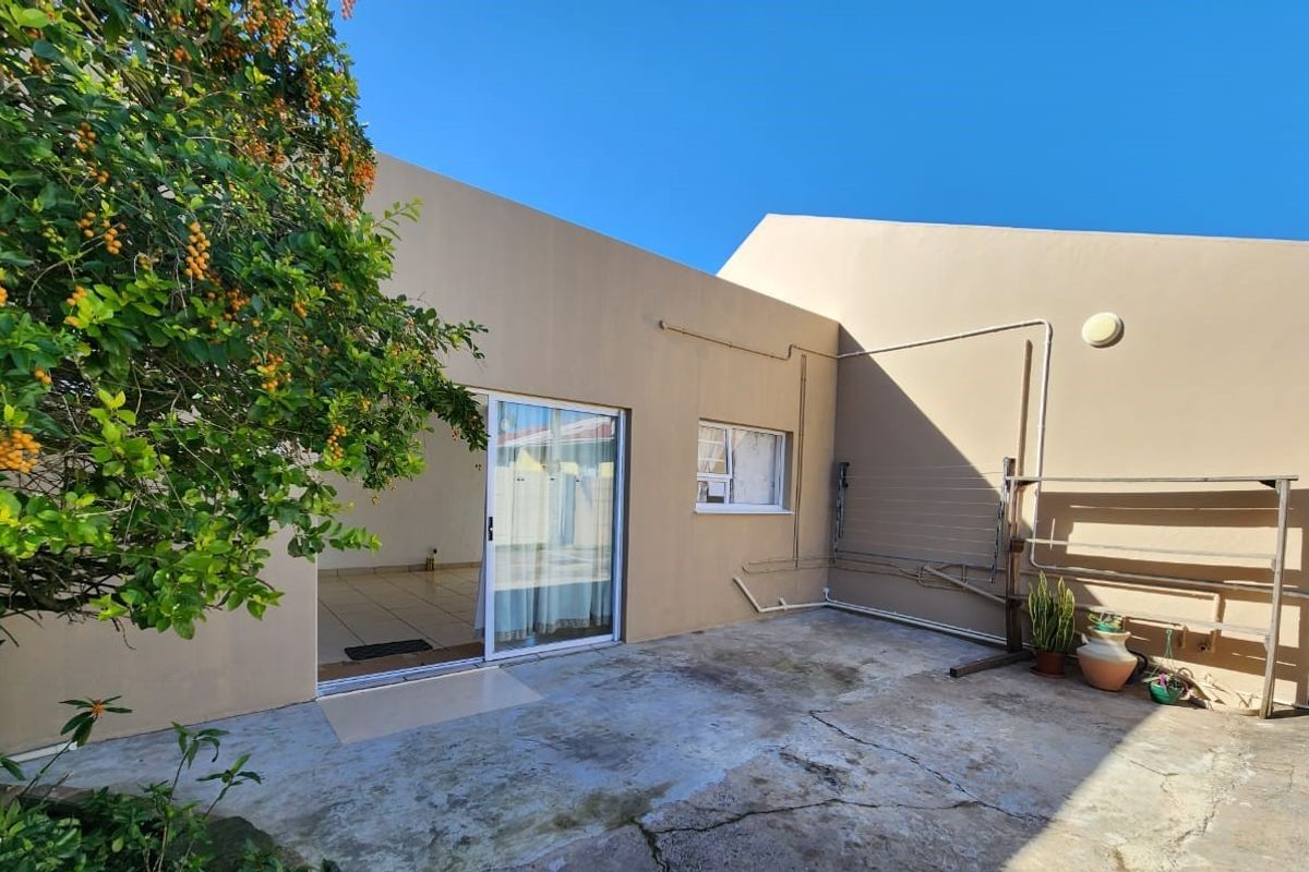 A rear exterior view of the flat featuring a concrete patio area, sliding door access, and wall-mounted drying rack.