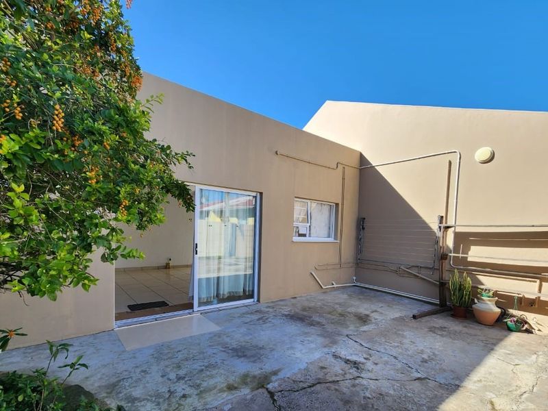 A rear exterior view of the flat featuring a concrete patio area, sliding door access, and wall-mounted drying rack.
