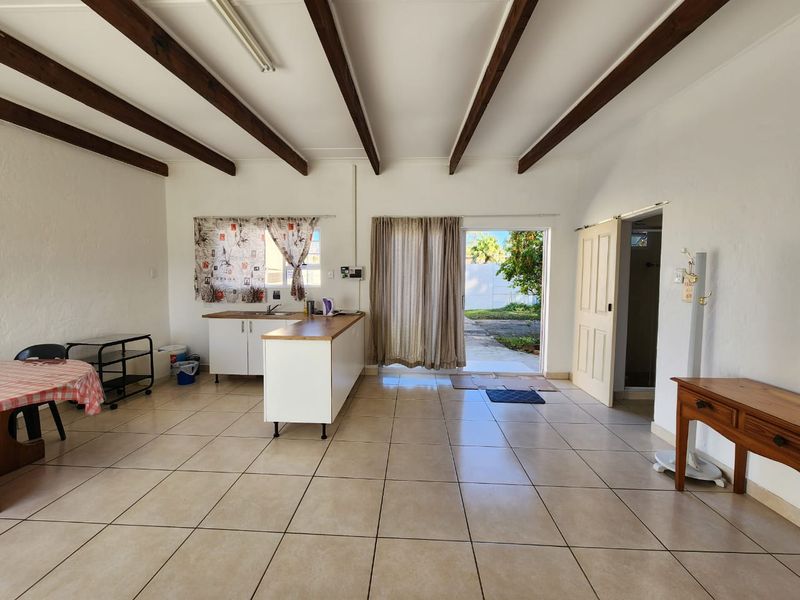 Open-plan living area featuring exposed timber ceiling beams, tiled flooring, and a functional kitchen space with direct access to the outdoor area.