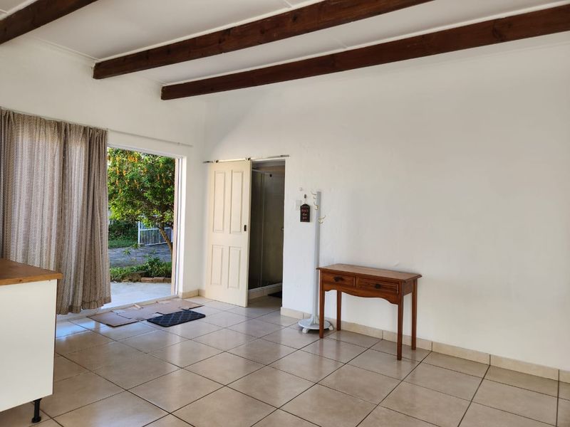 Open plan living area featuring exposed timber ceiling beams, ceramic tiled flooring, and direct access to an outdoor patio area.