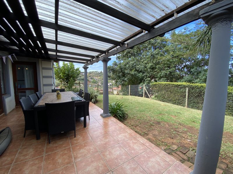Covered outdoor patio featuring tiled flooring and a pergola structure, overlooking a private garden area.
