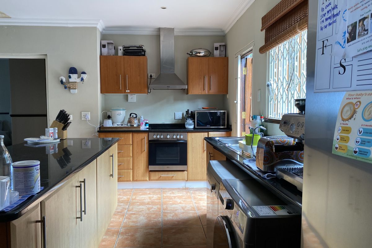 Functional kitchen featuring wooden cabinetry, granite countertops, built-in oven with extractor fan, and tiled flooring with direct access to the exterior.