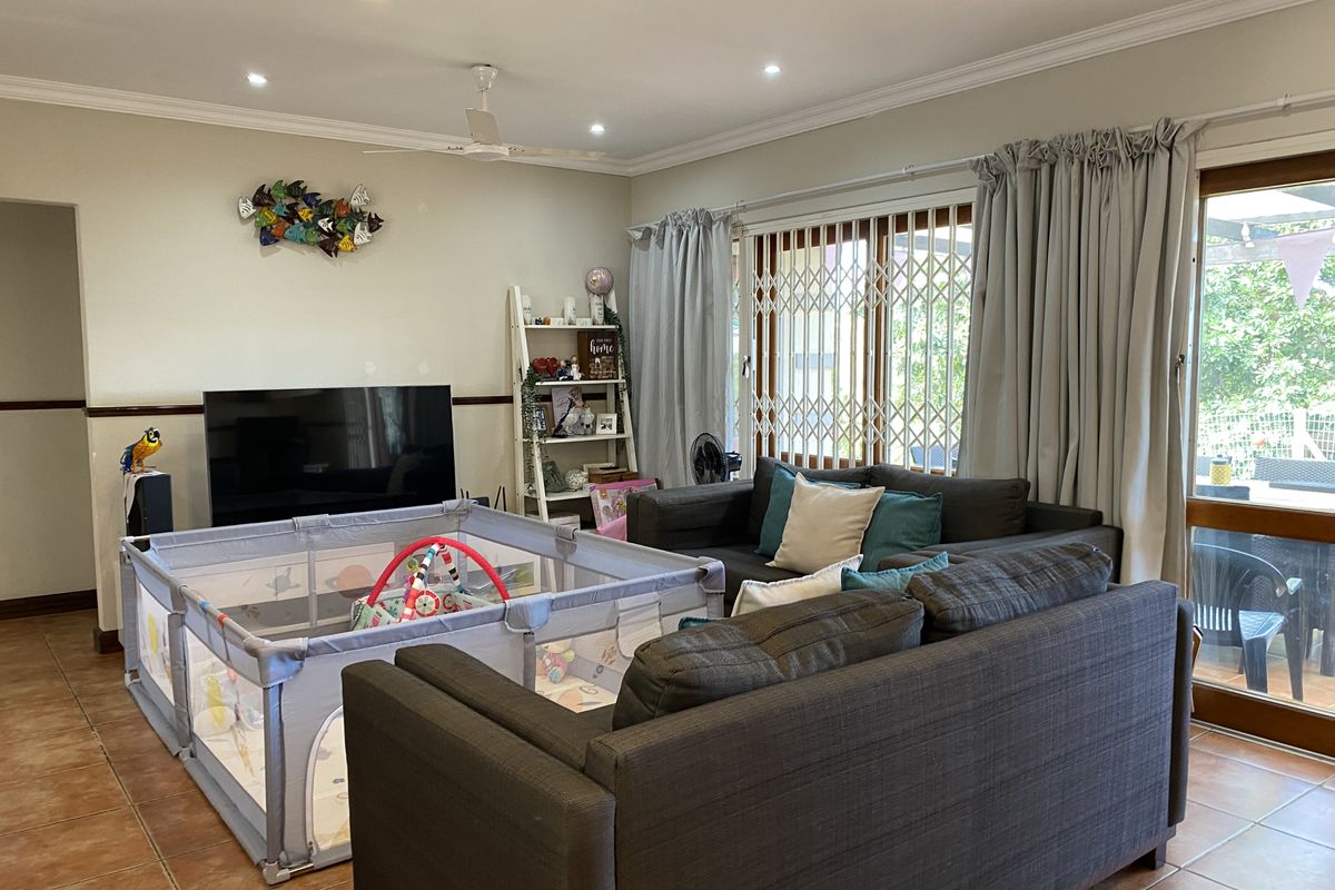 A spacious living room featuring tiled flooring, recessed downlighting, and a sliding glass door with security gate providing access to the outdoor area.