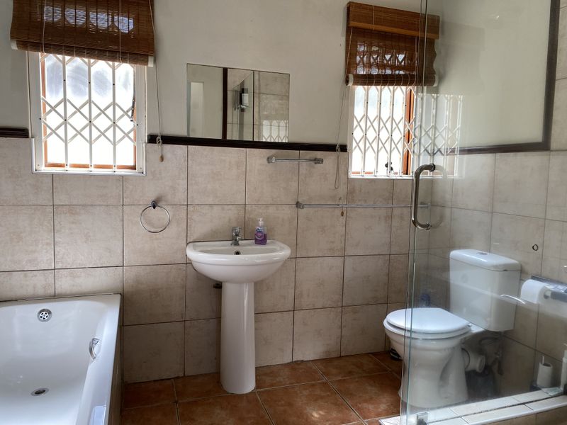 A functional bathroom featuring a pedestal basin, bathtub, and a separate glass-enclosed shower with neutral wall and floor tiling.