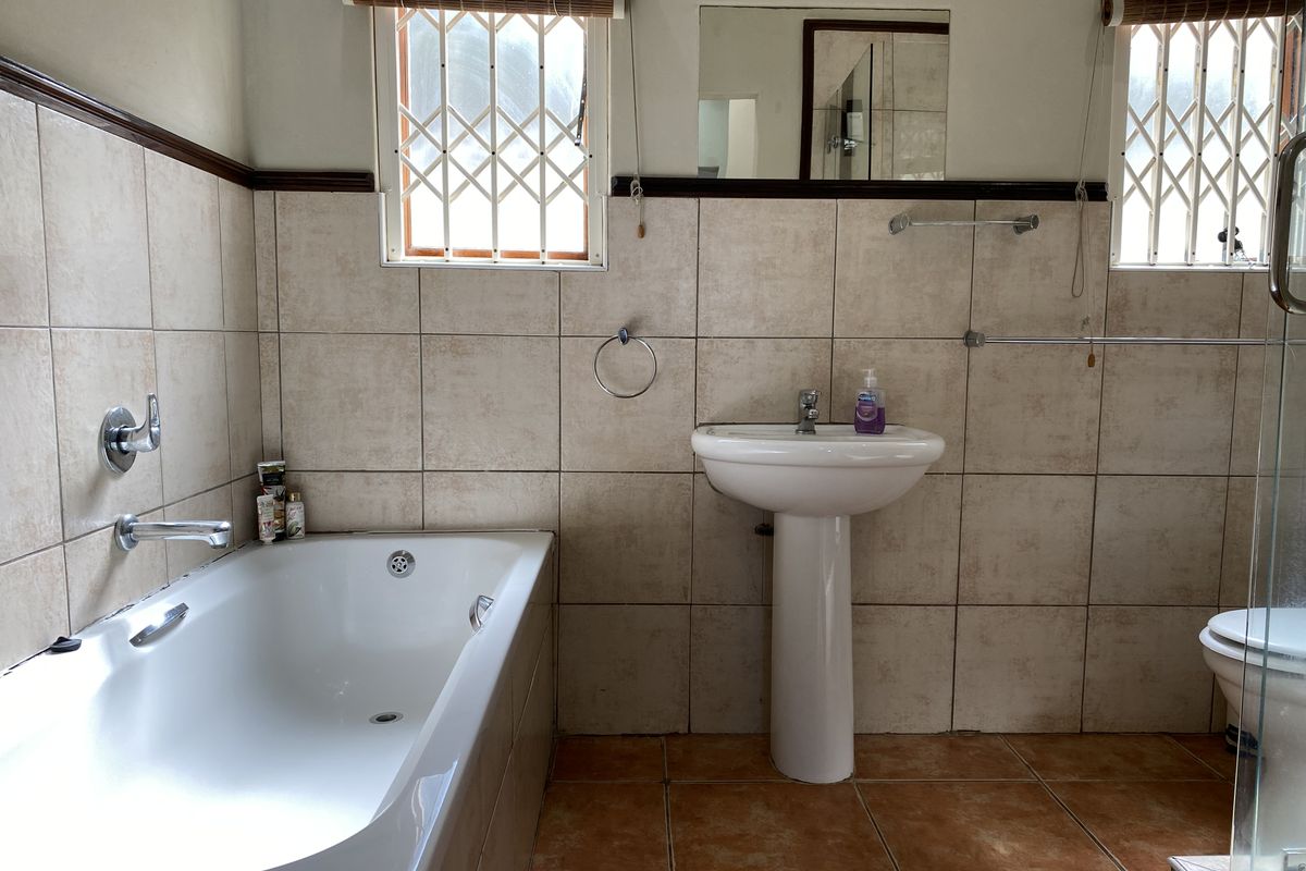 A functional bathroom featuring a pedestal basin, built-in bathtub, and toilet, finished with neutral ceramic wall tiles and terracotta-toned floor tiles.