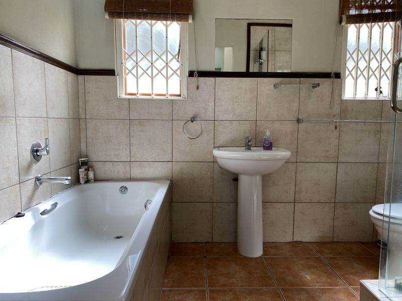 A functional bathroom featuring a pedestal basin, built-in bathtub, and toilet, finished with neutral ceramic wall tiles and terracotta-toned floor tiles.