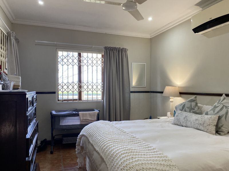 A comfortable bedroom featuring tiled flooring, crown molding, a ceiling fan, and a wall-mounted split-system air conditioner for climate control.
