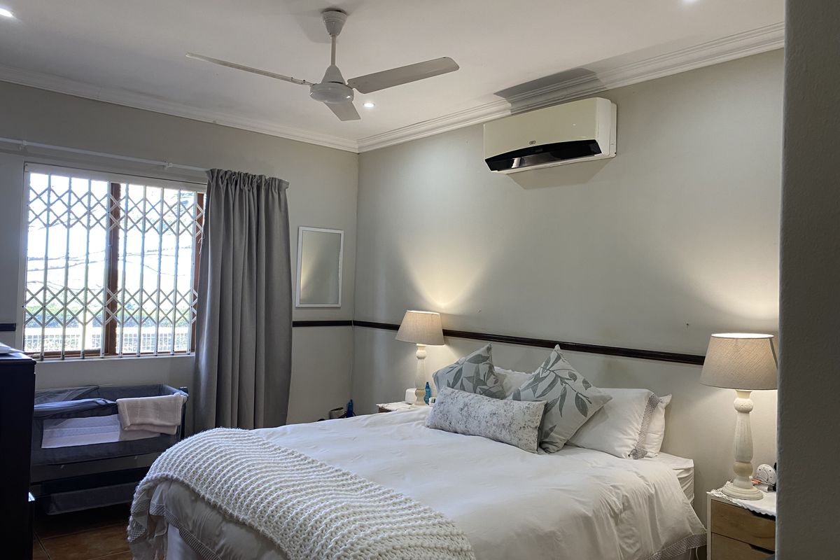 A well-maintained bedroom featuring a ceiling fan, split-system air conditioning, recessed lighting, and a security gate on the window.
