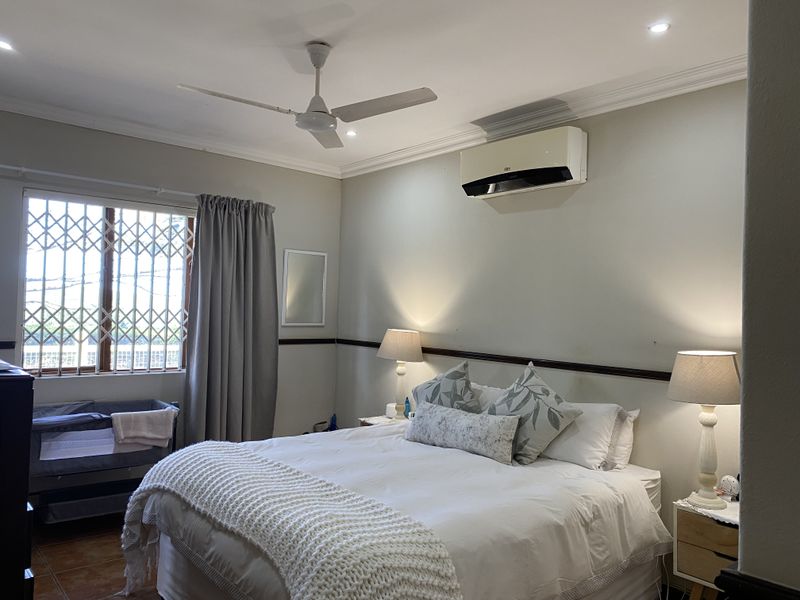 A well-maintained bedroom featuring a ceiling fan, split-system air conditioning, recessed lighting, and a security gate on the window.