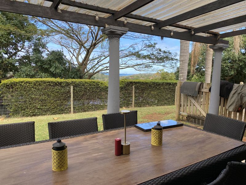 Covered outdoor patio area featuring a pergola structure with columns, overlooking a garden and distant landscape views.
