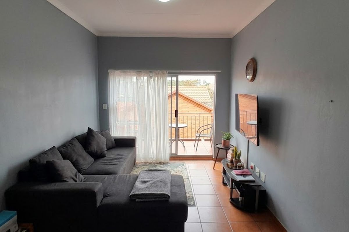 A comfortable living room featuring tiled flooring and a sliding glass door that opens onto a private balcony.