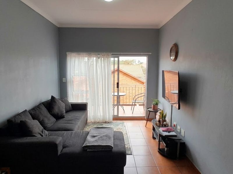 A comfortable living room featuring tiled flooring and a sliding glass door that opens onto a private balcony.
