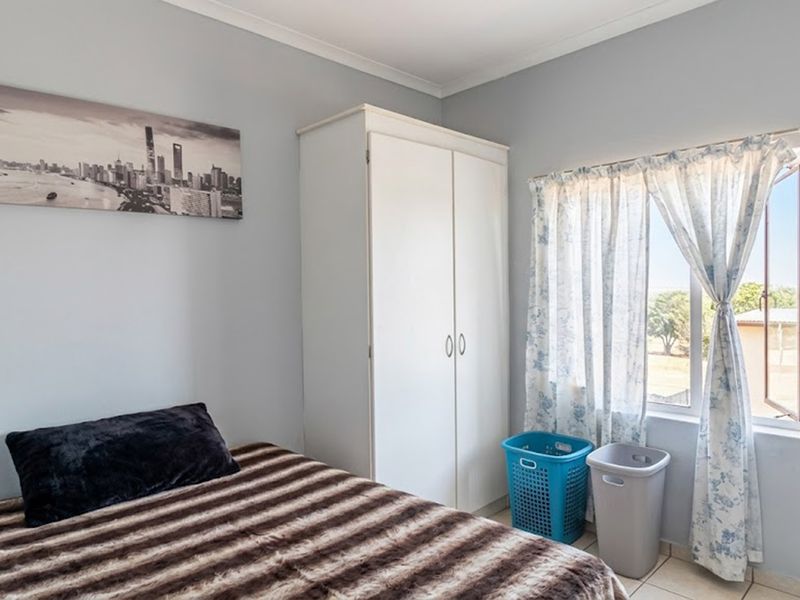 A functional bedroom featuring tiled flooring, a built-in wardrobe, and a window providing natural light.