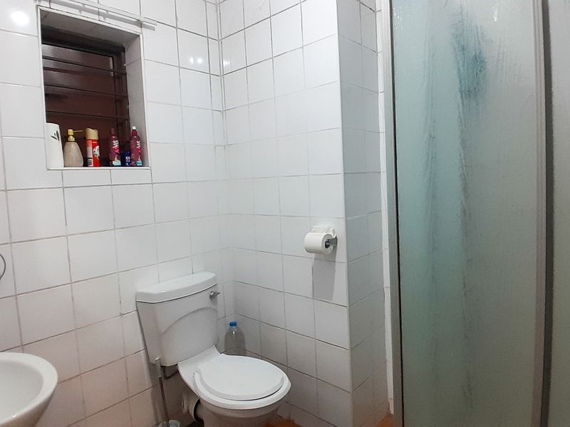 A functional bathroom featuring white wall tiles, a pedestal basin, a standard toilet, and a glass shower enclosure.