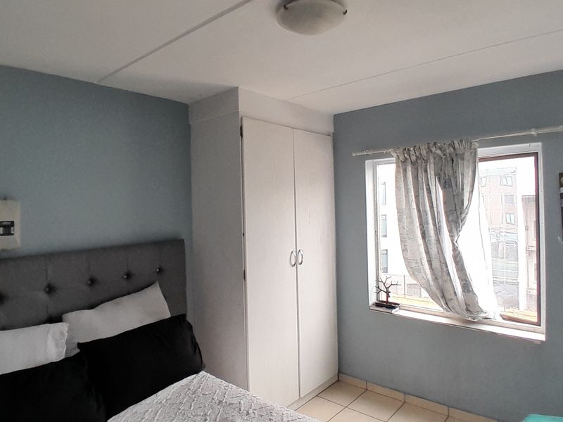 A functional bedroom featuring a built-in wardrobe, tiled flooring, and a window providing natural light.