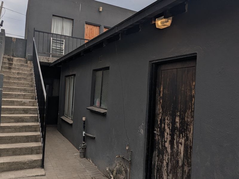 Rear exterior view of the apartment building featuring a paved courtyard, external staircase, and weathered wooden door access.