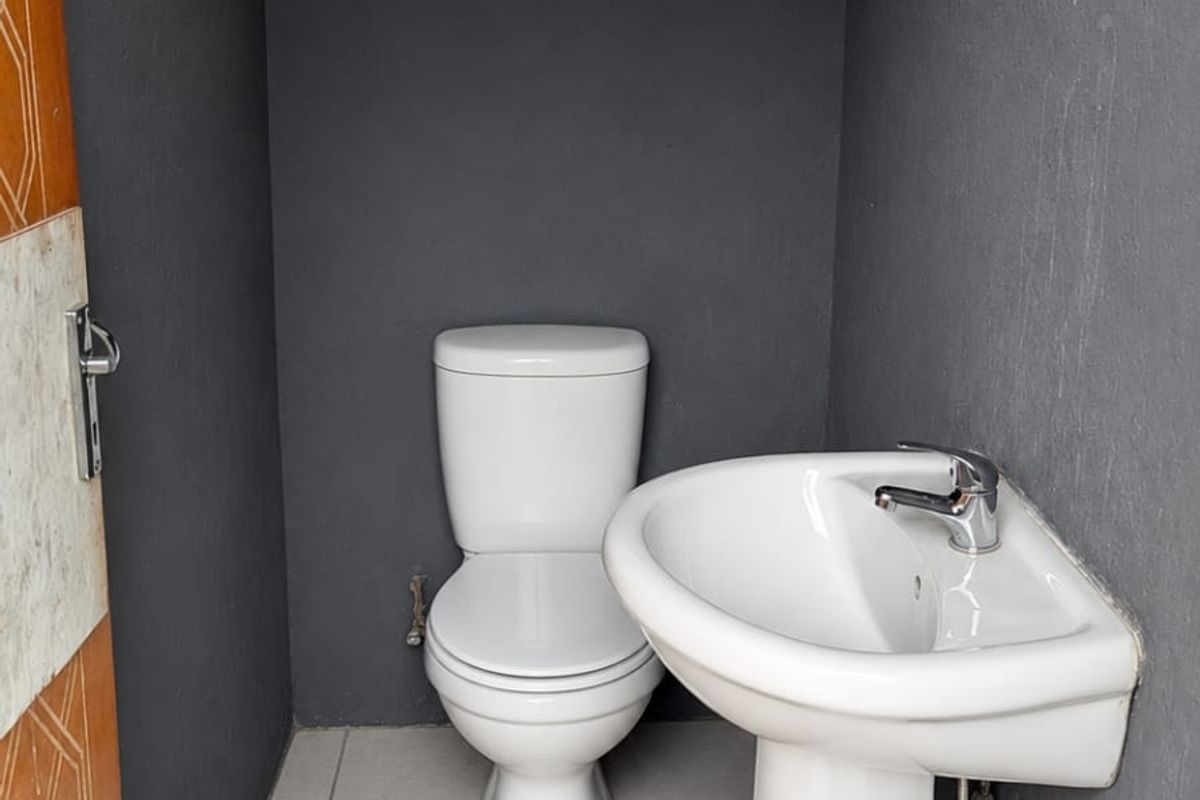 A small, minimalist bathroom featuring a white pedestal basin and toilet against dark grey walls with light floor tiles.