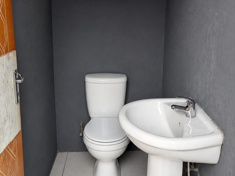 A small, minimalist bathroom featuring a white pedestal basin and toilet against dark grey walls with light floor tiles.