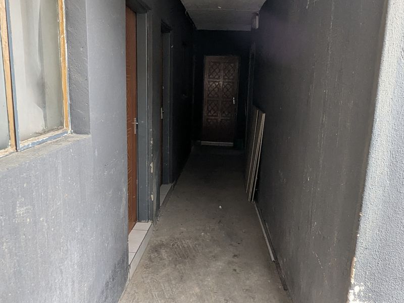 A narrow exterior hallway with dark painted walls, concrete flooring, and multiple door access points, showing signs of wear and requiring maintenance.