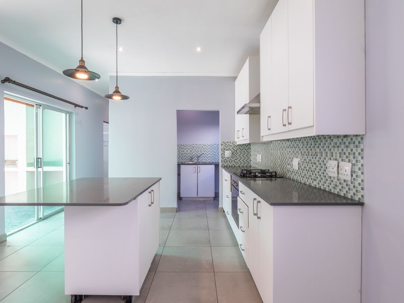 Modern kitchen featuring white cabinetry, stone countertops, gas hob, built-in oven, and a mosaic tile backsplash, with an adjacent scullery area.