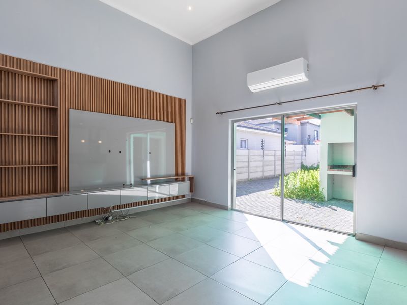 Spacious living room featuring modern slatted wood wall paneling, built-in cabinetry, tiled flooring, and a sliding glass door leading to the outdoor area.