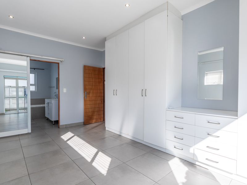 Spacious bedroom featuring neutral tiled flooring, built-in cupboards, recessed lighting, and an integrated air conditioning unit, with direct access to an en-suite bathroom.