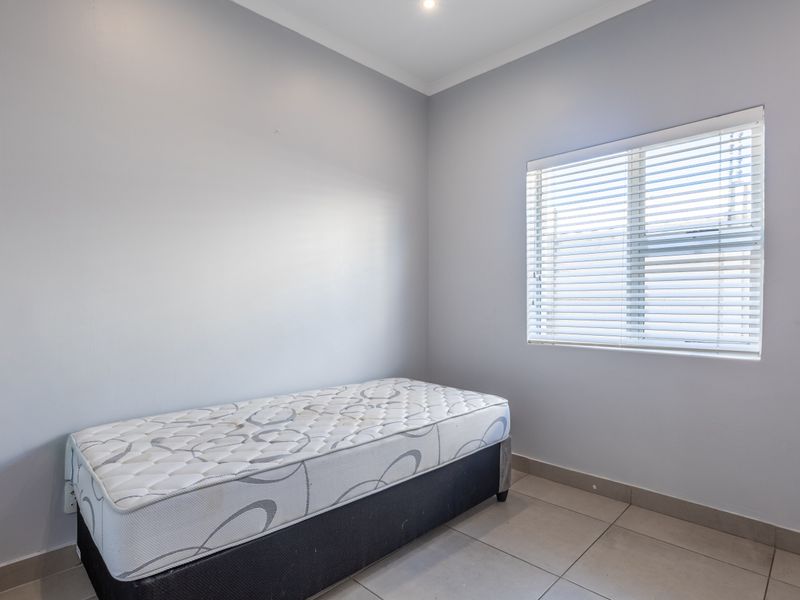 A clean, neutral-toned bedroom featuring tiled flooring, cove cornicing, and a window fitted with venetian blinds.