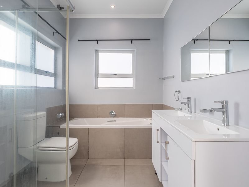 A modern, well-maintained bathroom featuring a double vanity, a built-in bathtub, and a separate glass-enclosed shower with neutral tile finishes.