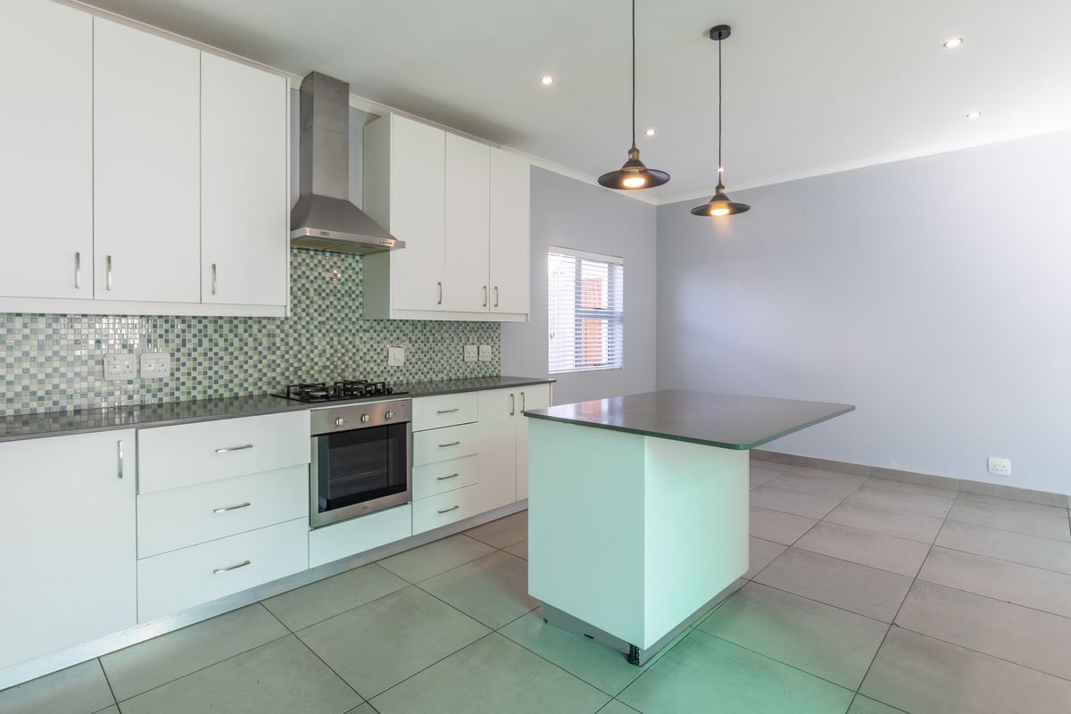 Modern kitchen featuring white cabinetry, a mosaic tile backsplash, stainless steel appliances, a central island, and neutral tiled flooring in an open-plan layout.