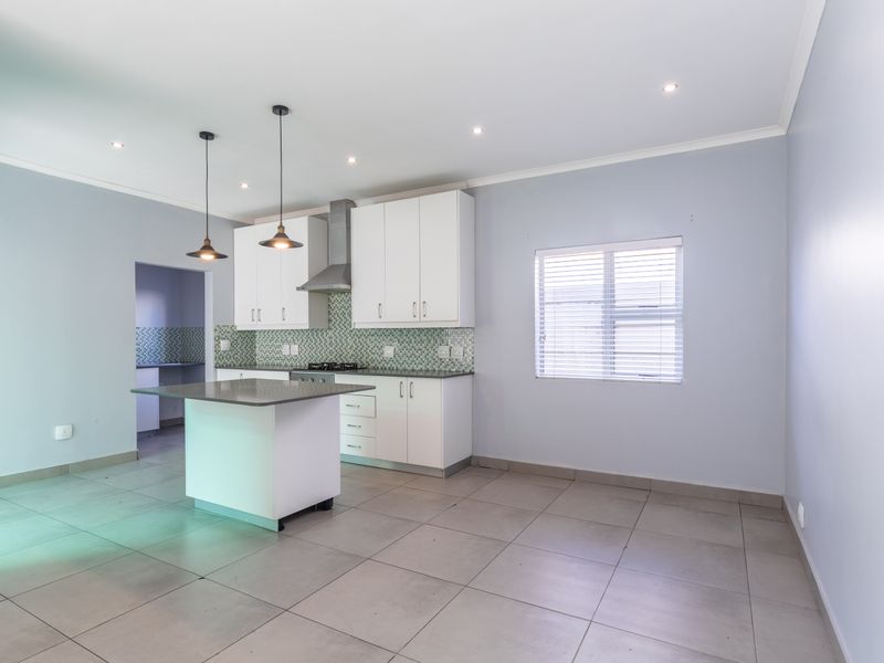 Modern kitchen featuring a central island, white cabinetry, tiled splashback, and neutral floor tiles, offering a clean and functional space.