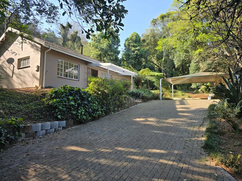 Front exterior view of the house featuring a paved driveway, carport, and established garden surroundings.
