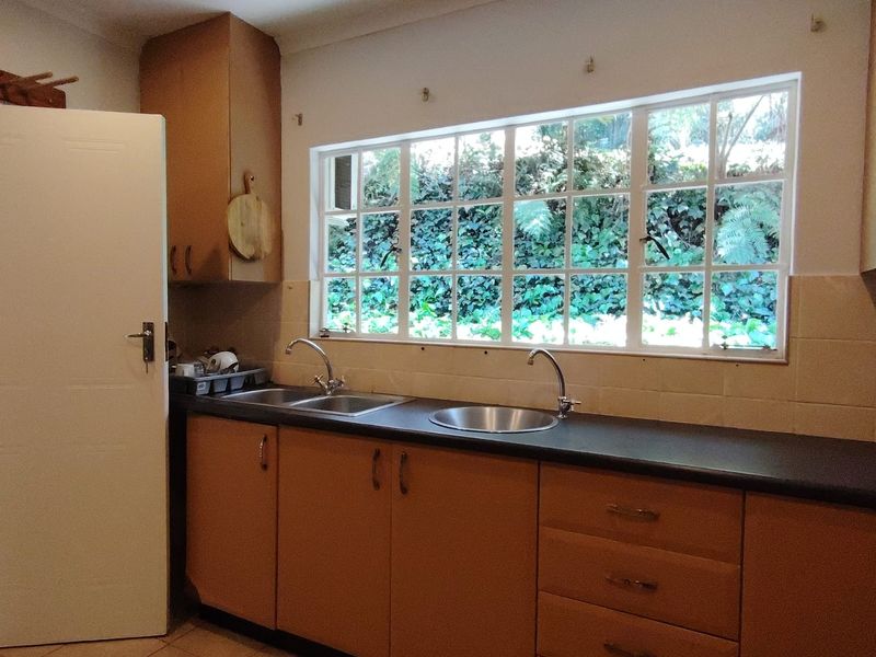 A functional kitchen featuring laminate cabinetry, a double stainless steel sink, tiled backsplash, and a large window overlooking the garden.
