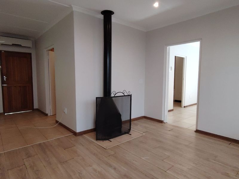 An open-plan living area featuring wood-look tile flooring, a central freestanding fireplace, and recessed downlighting, presenting a clean and neutral blank canvas.