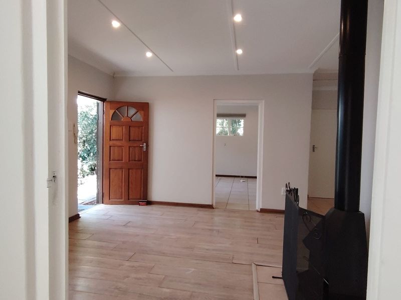 An empty, well-lit living room featuring modern laminate flooring, a built-in wood-burning fireplace, and direct access to the front entrance.