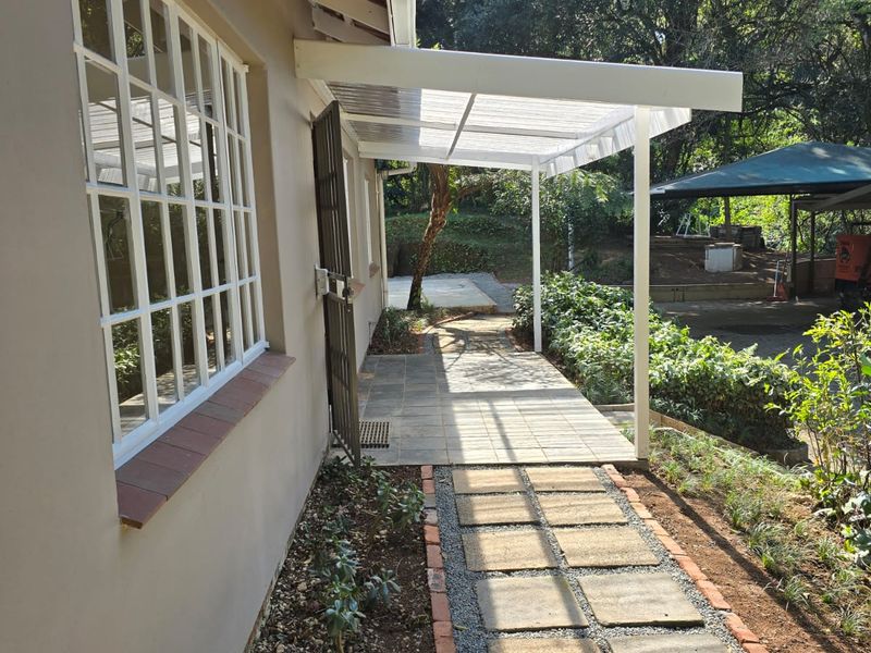 A well-maintained rear exterior view featuring a covered patio area, paved walkway, and established garden surroundings.