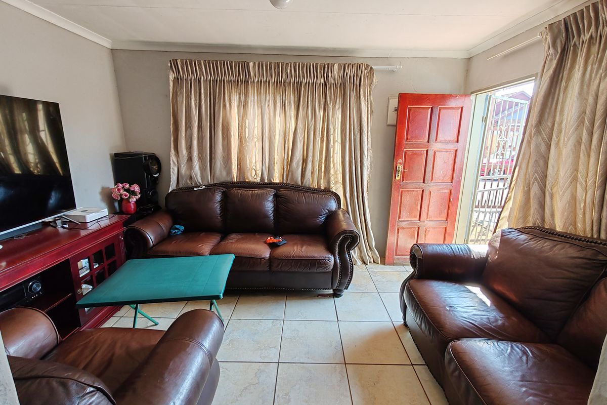 A functional living room featuring tiled flooring, a solid wood entrance door with security gate, and neutral wall finishes.